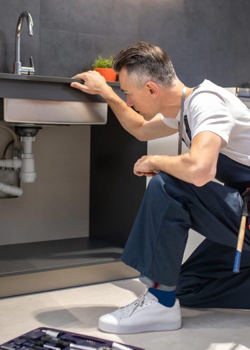 man-kneeling-down-touching-sink-inspecting-pipes